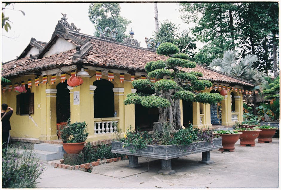 A traditional yellow house adorned with lanterns and surrounded by lush greenery and bonsai trees.