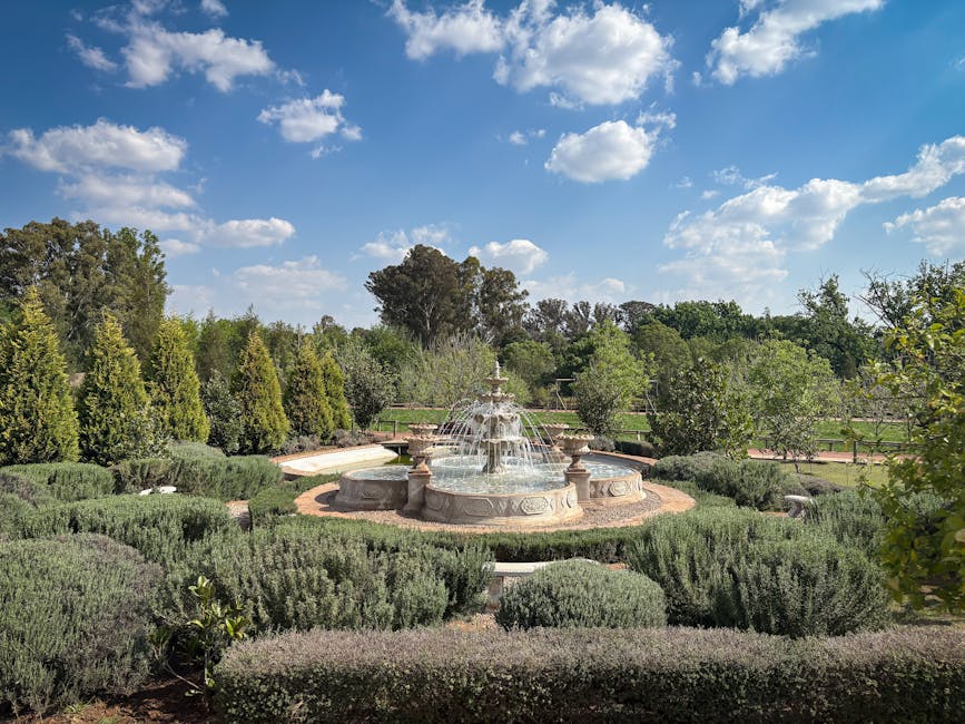 Tranquil stone fountain surrounded by greenery under a bright blue sky in a lush garden.