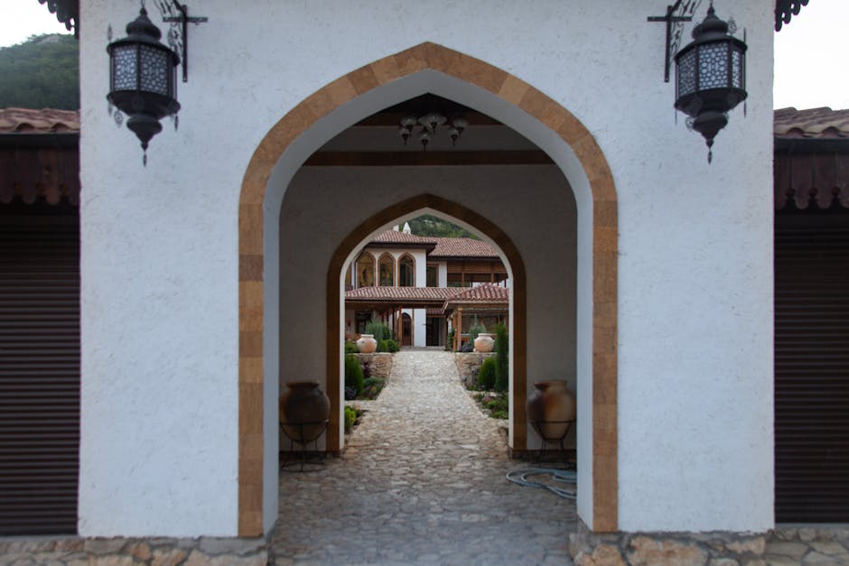 Picturesque cobblestone path leads through Mediterranean archway to a villa.